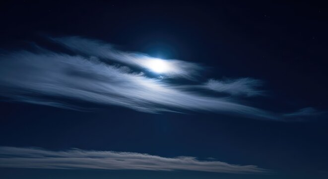 Wispy silver clouds drift slowly across a vast dark indigo sky, illuminated by the soft glow of a hidden moon during a peaceful midnight, twilight, light, landscape