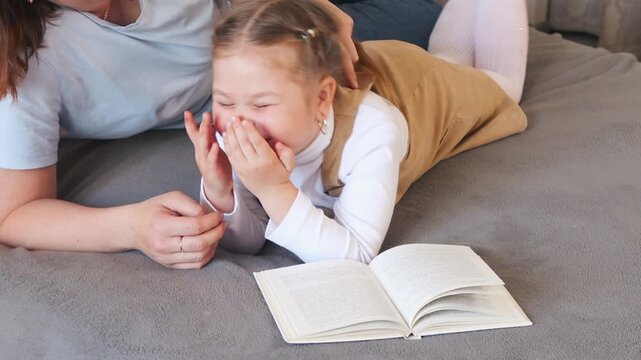 Preschool age girl explores reading while her mom guides her through a story. Supportive early childhood education. Close up