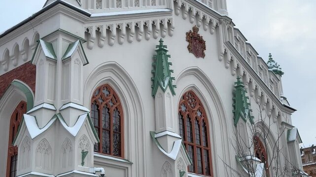 Close up view of a white Gothic church facade with pointed arches and green spires covered in winter snow.