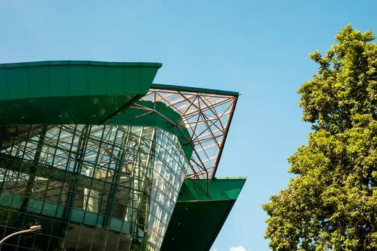 A unique contemporary glass architecture of university graduation building in Jember Indonesia with green summer foliage and blue sky background during summer.