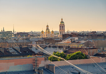 St. Petersburg rooftops glow under golden hour light, showing historic church domes and a distant spire © Evgenii Bakhchev