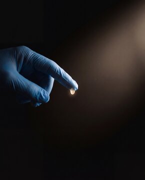 Minimal Dark Background Gloved Hand with Glowing Translucent Liquid Droplet in Laminar Flow Hood