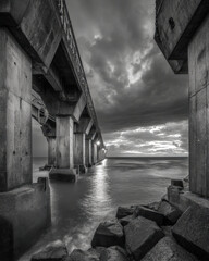 Obraz premium Black and White Concrete Seawall Under Storm Clouds with Rough Water