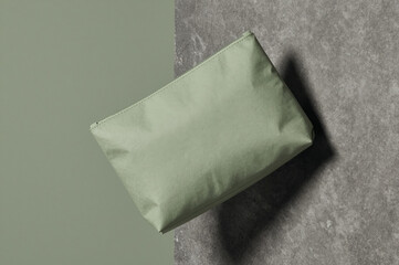 Naklejka premium Pouch rests on a split surface composed of sage green matte and gray concrete texture under soft diffused light from above. Its rectangular shape creates sharp diagonal lines across the frame.