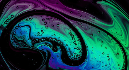 Fototapeta premium Iridescent petroleum stain swirling in dark fluid with vibrant green blue and purple color showcasing organic ink flow pattern shimmering oily surface and microscopic bubble in black water.