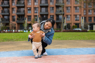 Obraz premium Happy mother helping her baby son take first steps outdoor