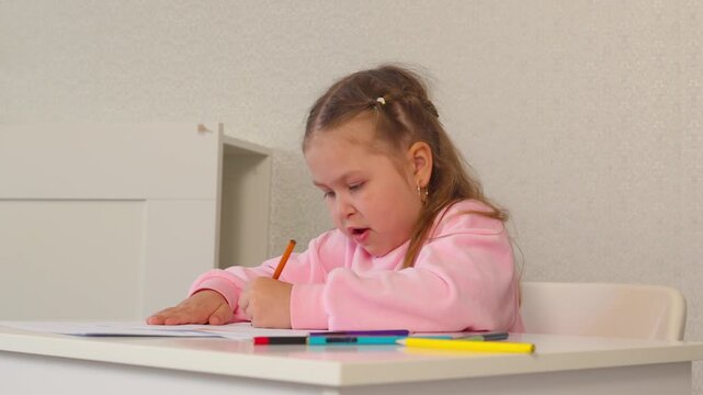 Caucasian girl focuses on drawing shapes and coloring within the lines. Preschool activity for developing coordination.