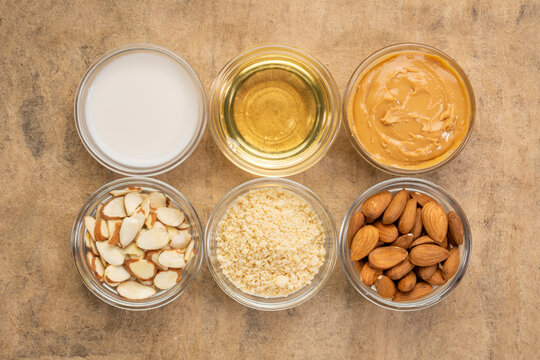 collection of almond super foods: nuts, flour,  milk, oils and butter - top view of small glass bowls over textured bark pape