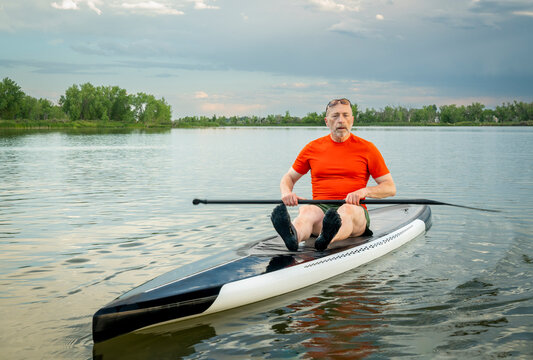 senior man sitting on a stand up paddleboard, spring lake scenery in Colorado.