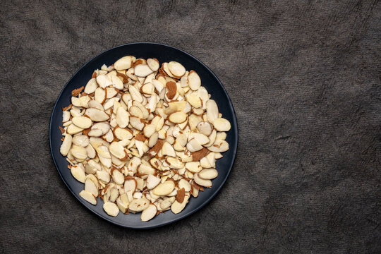 almond slices and on a black plate against textured  bark paper with a copy space
