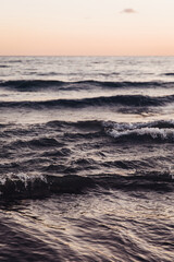 Obraz premium Close-up of dark, moody ocean waves rolling and breaking near the shore. Textured water surface and sea foam reflect soft, warm light of twilight, creating a dramatic and abstract marine background.
