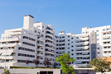 Modern apartment complex featuring white contemporary residential architecture, balconies and landscaped surroundings in a newly developed urban district under a clear blue sky. © Jorge