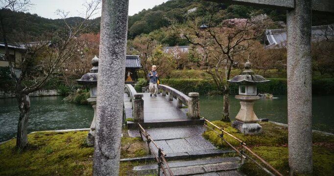Beautiful rain storm as little boy walks across stone bridge near torii gate in Japanese village