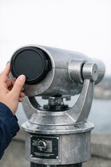 Obraz premium A person operating a coin-operated telescope near the water's edge, ideal for use in travel or educational settings