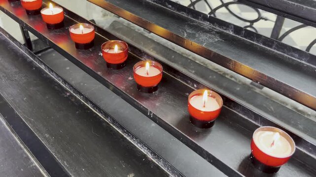 Memorial candles burn on shelf in ancient European cathedral