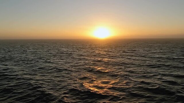 Calm ocean view from a sailing boat at sunset, with golden light reflecting on gentle waves. The horizon glows with warm colors, creating a peaceful and serene atmosphere of travel and freedom