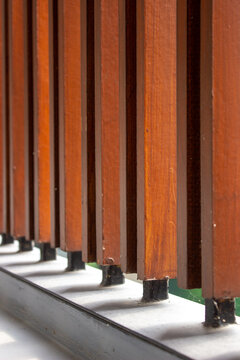 Vertical rows of teak wooden louvers with outdoor finishing neatly installed on a minimalist building iron railing.
