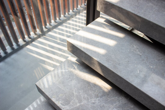 Modern floating staircase with gray marble stone steps receiving linear shadow lines pattern from window louvers.