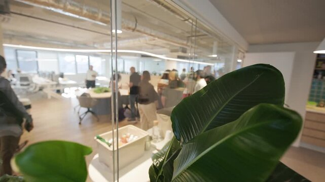 Group of diverse professionals engaged in collaborative discussion inside a modern office space with large windows and greenery visible in the foreground