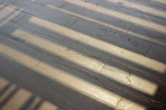 Gray tile floor texture with horizontal geometric shadow patterns from afternoon sunlight in an outdoor terrace area.