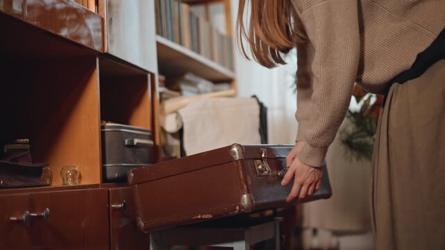 Caucasian woman opening linen filled suitcase, pulling out embroidered cloth and heirloom textiles, seamstress granddaughter scene, gentle smile and cozy ambient light, affectionate family moment