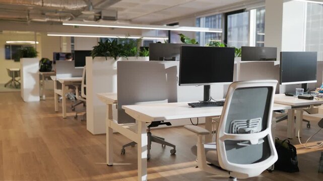 Modern office workspace with multiple desks and computers, showcasing a clean and organized environment with plants and natural light streaming through large windows