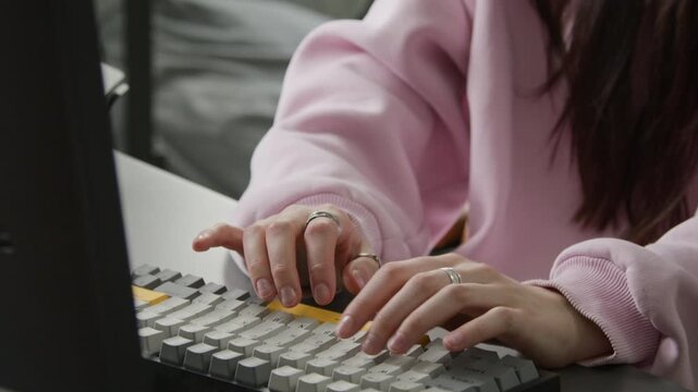 Tilting close-up of hands and face of young Caucasian female programmer writing computer script with vibe coding, typing commands on keyboard, looking at screen to check result, straightening glasses