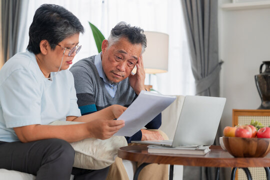 Senior Asian couple reviewing financial documents and bills with laptop computer at home concept for retirement planning savings account budget debt tax form insurance expenses