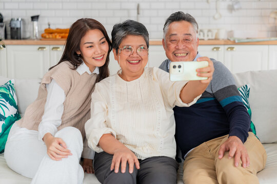 Happy Asian family taking a selfie with smart phone inside home kitchen concept for social media photo digital influencer technology marketing lifestyle happiness