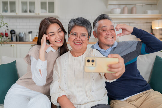 Happy Asian family taking a selfie with smart phone inside home kitchen concept for social media photo digital influencer technology marketing lifestyle happiness
