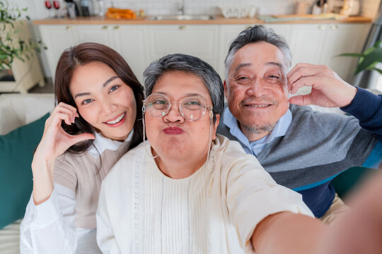 Happy Asian family taking a selfie with smart phone inside home kitchen concept for social media photo digital influencer technology marketing lifestyle happiness