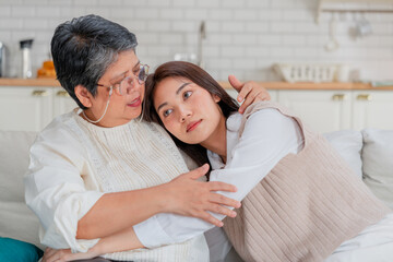 Obraz premium Adult Asian daughter leaning on senior mother shoulder for emotional support health insurance marketing campaign tender family bonding authentic relationship portrait living room home studio