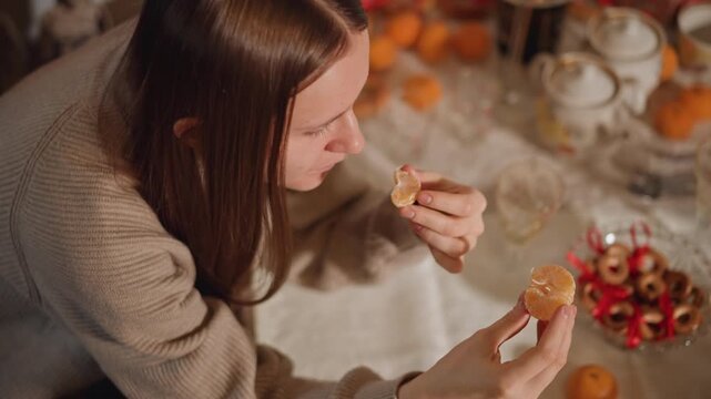 Woman sampling pastry at holiday table, teapot and ornaments in frame, warm overhead composition, candid blogger tasting cookie, seasonal treats and citrus accents, cozy kitchen vibe