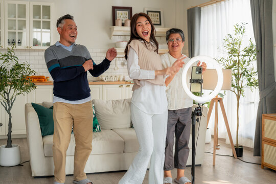 Active Asian multi-generation family dancing together for short video content online with smart phone and ring light inside home living room concept for social media challenge influencer 