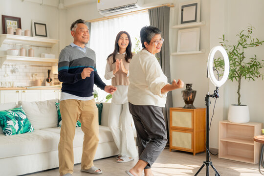 Active Asian multi-generation family dancing together for short video content online with smart phone and ring light inside home living room concept for social media challenge influencer 