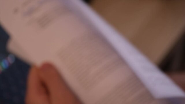 Man Reviewing Printed Documents and Turning Pages Close Up. The document content remains intentionally out of focus, making the footage suitable for a wide range of business, administrative, legal, fi