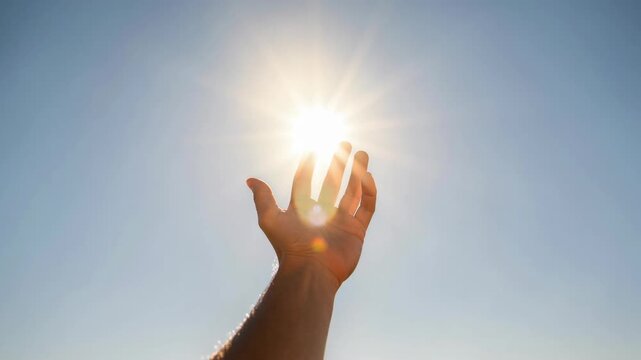 Human hand reaching towards bright sun in clear sky symbolizing hope and energy