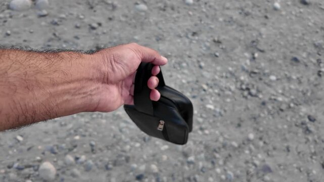 Black PU leather men&rsquo;s clutch with wristlet strap and zippered pocket outdoors in nature.