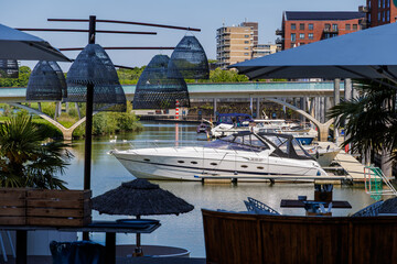 Naklejka premium Luxury yacht at marina viewed from waterfront terrace with umbrellas and city skyline.