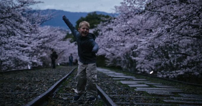 Funny, dancing boy on old tracks and surrounded by spring cherry blossoms in Japan