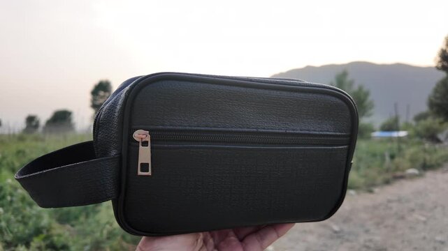 Black PU leather men&rsquo;s clutch with wristlet strap and zippered pocket outdoors in nature.