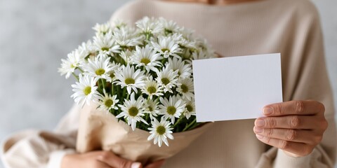 Obraz premium A beautiful bouquet of daisies in a person's hands accompanied by a blank card, symbolizing warmth, love, and the perfect gesture for greeting someone special.