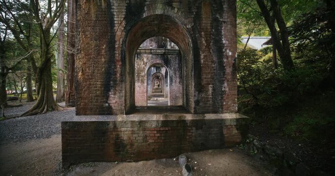 Long row of brick arches under old Japanese bridge in forest - slow motion steady cam