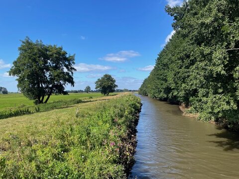 Eine Br&uuml;cke f&uuml;hrt &uuml;ber den Fluss Varreler B&auml;ke. B&auml;ume stehen am Fluss. Dieser ist die Landesgrenze zwischen Bremen und Niedersachsen. Es ist ein sonniger Sommertag.  