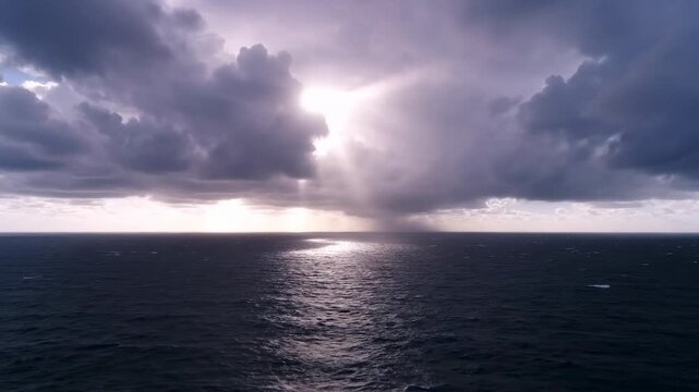 Sunlight breaks through dark clouds illuminating ocean waves. Stormy atmosphere captures early morning setting over open water. Concept of nature, weather, coastal exploration