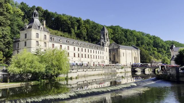 Scenic view of Brant&ocirc;me Abbey beside the Dronne River as visitors walk across the bridge. Historic architecture and tourism in the heart of the Dordogne region.