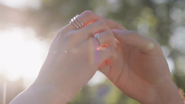 Two people man and woman gently touching and holding each other's hands in warm natural sunlight. Romantic gesture between partners highlighting tenderness, care, engagement, marriage and connection