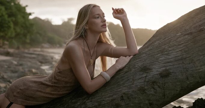 Portrait of young blonde woman posing on wooden log at beach