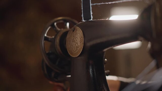 Antique sewing machine closeup hand guiding fabric wheel in warm workshop light, needle and bobbin visible, focus on metal patina and textured thread, quiet careful tailoring scene