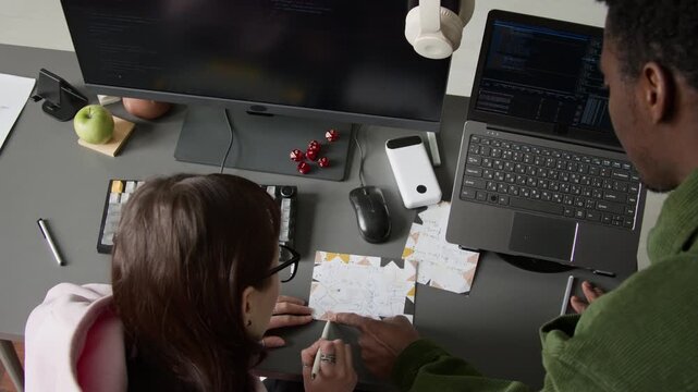 Top view of female Caucasian and male African American software developers brainstorming while drawing block scheme at desk, discussing and planning work on project, computer code on screens